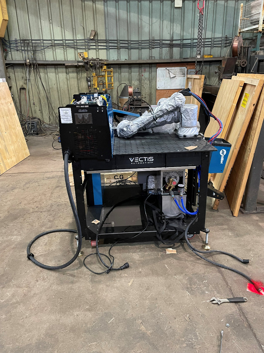 A Partly assembled robotic welding arm sits on the table that it will weld on. In the background are the remains of the shipping crate the device arrived in.